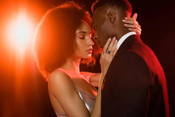 Curly african american woman in dress embracing man on black — Stock Photo