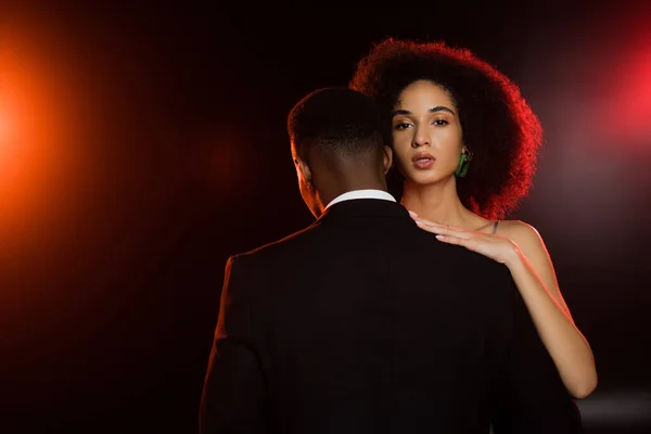 Elegant african american woman embracing man in suit on black — Stock Photo