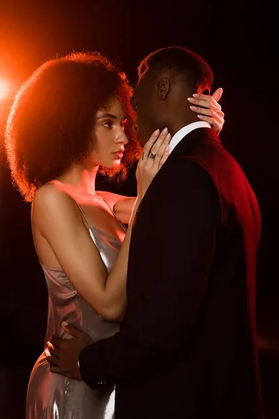 Elegant african american woman in dress embracing man on black — Stock Photo