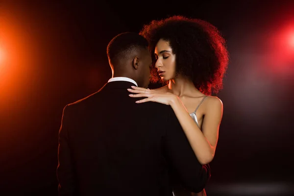 Elegante donna afroamericana che abbraccia l'uomo in abito formale su nero — Foto stock