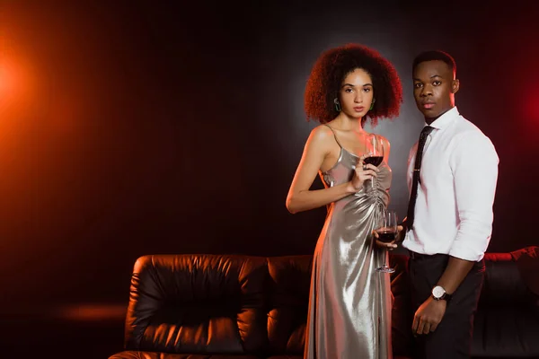 Curly african american woman and man holding glasses of red wine on black — Stock Photo