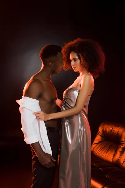 Curly african american woman in dress taking off shirt on man on black — Stock Photo