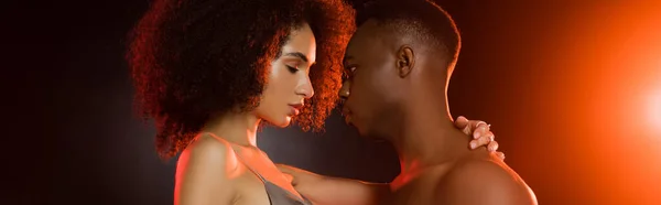 Side view of shirtless african american man seducing curly woman on black, banner — Stock Photo