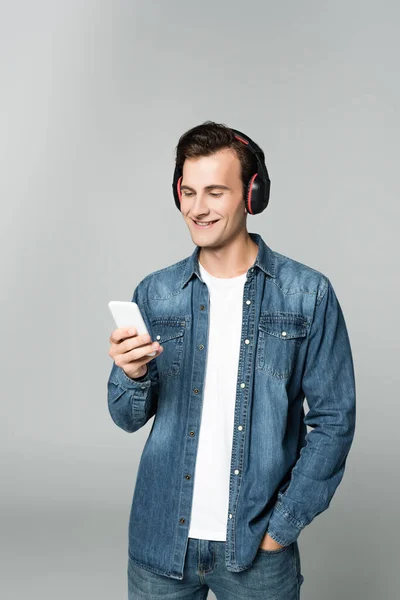 Homem sorridente em fones de ouvido usando smartphone isolado em cinza — Fotografia de Stock