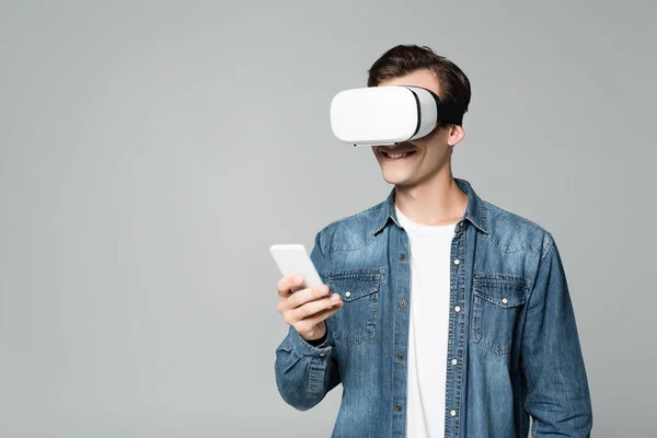 Sonriente hombre vr auriculares usando teléfono inteligente aislado en gris - foto de stock