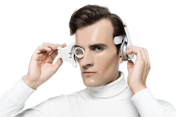 Cyborg olhando para a câmera ao tocar lente de olho digital e fones de ouvido isolados em branco — Fotografia de Stock