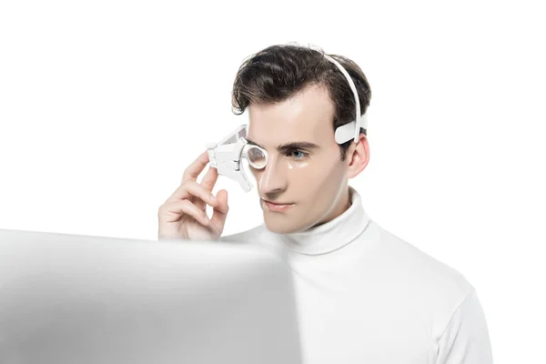 Cyborg in eye lens and headphones looking at computer on blurred foreground isolated on white — Stock Photo