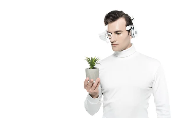 Cyborg man in white clothes, headphones and eye lens looking at potted plant isolated on white — Stock Photo