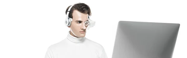 Brunette cyborg man in headphones and eye lens looking at computer monitor isolated on white, banner — Stock Photo