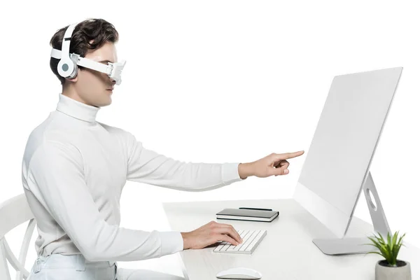 Cyborg in headphones and eye lens pointing at computer near notebook and plant on blurred foreground isolated on white — Stock Photo