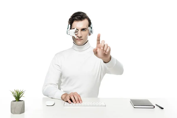 Cyborg en auriculares y lente para los ojos tocando algo y utilizando el teclado de la computadora cerca del portátil y la planta aislada en blanco - foto de stock