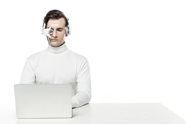 Cyborg em fones de ouvido e lente de olho digital usando laptop isolado em branco — Fotografia de Stock