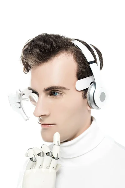 Cyborg em fones de ouvido e lente de olho digital tocando queixo com mão artificial isolada em branco — Fotografia de Stock