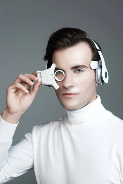 Brunette cyborg in headphones holding digital eye lens isolated on grey — Stock Photo