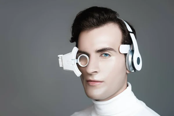 Cyborg en auriculares y lente de ojo mirando a la cámara aislada en gris - foto de stock