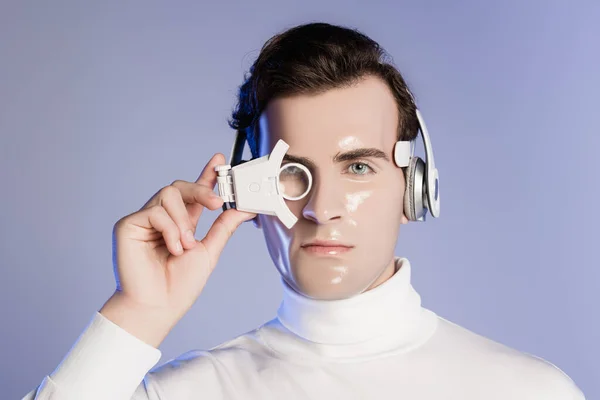 Homem ciborgue em fones de ouvido ajustando lente de olho digital isolado em roxo — Fotografia de Stock