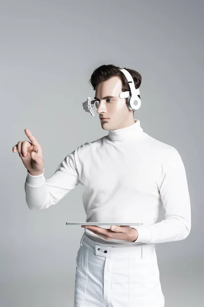 Cyborg en auriculares tocando algo y sosteniendo el teclado del ordenador aislado en gris - foto de stock