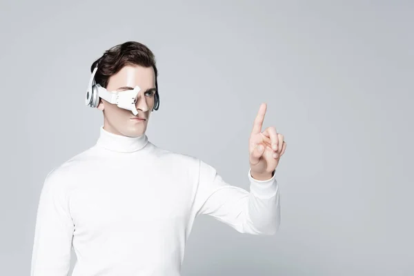 Cyborg in headphones and eye lens pointing with finger isolated on grey — Stock Photo