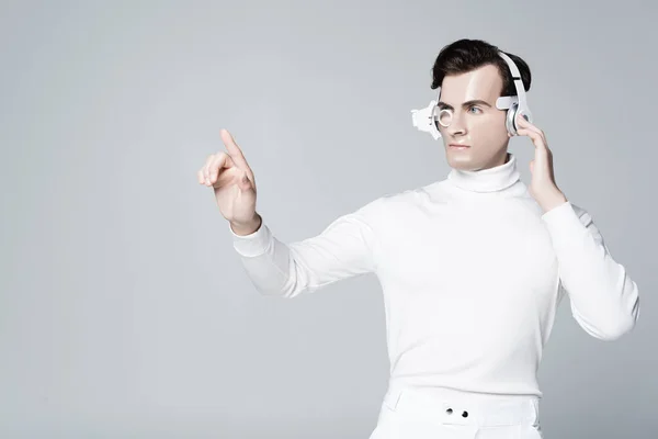 Cyborg homme dans les écouteurs toucher quelque chose et regarder loin isolé sur gris — Photo de stock