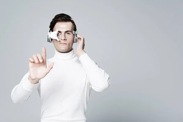 Cyborg mit einer Hand in der Nähe von Kopfhörern, die etwas Isoliertes auf Grau berührt — Stockfoto