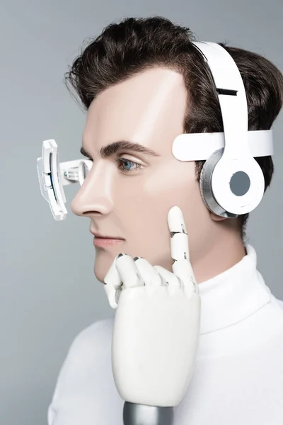 Cyborg man with headphones and finger of artificial hand near cheek isolated on grey — Stock Photo