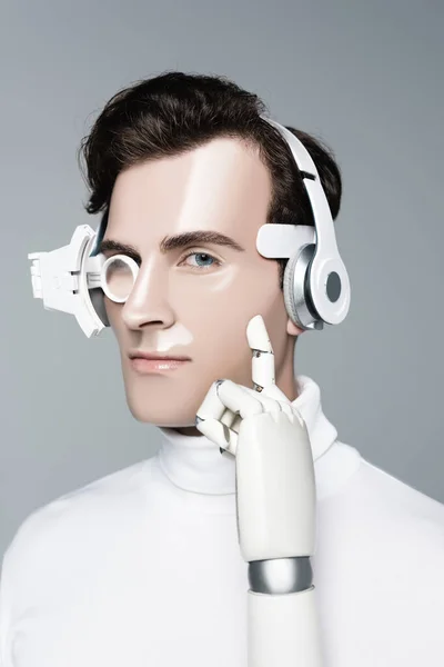 Cyborg en auriculares con mano artificial mirando a la cámara aislada en gris - foto de stock
