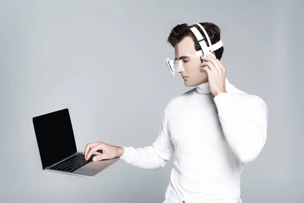 Ноутбук з порожнім екраном в повітрі біля кіборгу з навушниками ізольовані на сірому — стокове фото