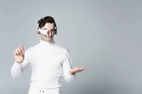 Cyborg im Kopfhörer berührt und zeigt auf etwas Isoliertes in Grau — Stockfoto