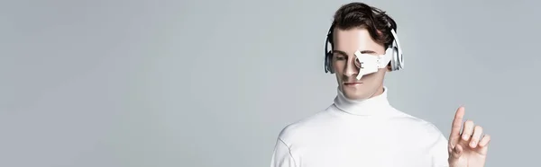 Cyborg hombre en auriculares apuntando con el dedo hacia arriba aislado en gris, bandera - foto de stock