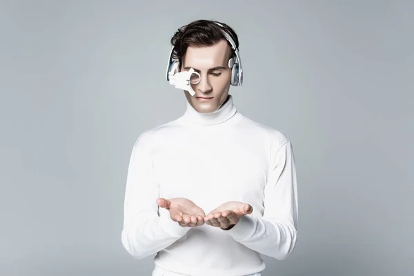 Cyborg em lente de olho digital e fones de ouvido segurando algo em mãos isoladas em cinza — Fotografia de Stock