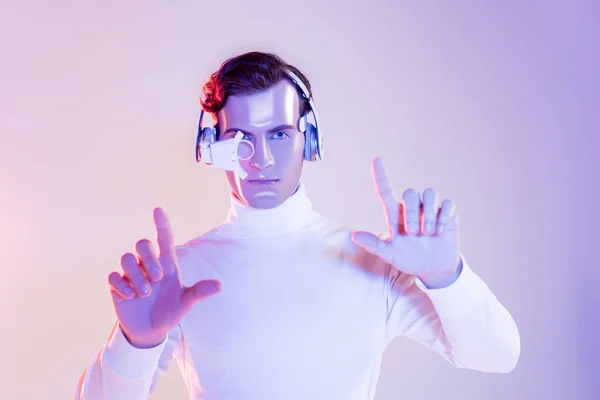 Cyborg dans la lentille oculaire et les écouteurs en utilisant quelque chose sur fond violet — Photo de stock