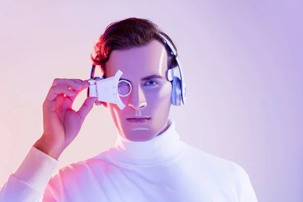 Brunette cyborg in headphones adjusting digital eye lens on purple background — Stock Photo