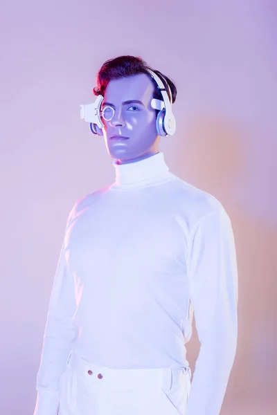 Cyborg en vêtements blancs et écouteurs regardant la caméra sur fond violet — Photo de stock