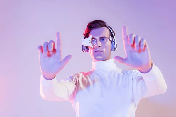 Cyborg bruna in lente oculare digitale e cuffie utilizzando qualcosa in primo piano sfocato su sfondo viola — Foto stock