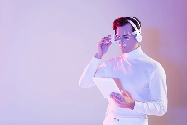 Cyborg mit Kopfhörer und digitaler Augenlinse, die ein digitales Tablet auf lila Hintergrund hält — Stockfoto