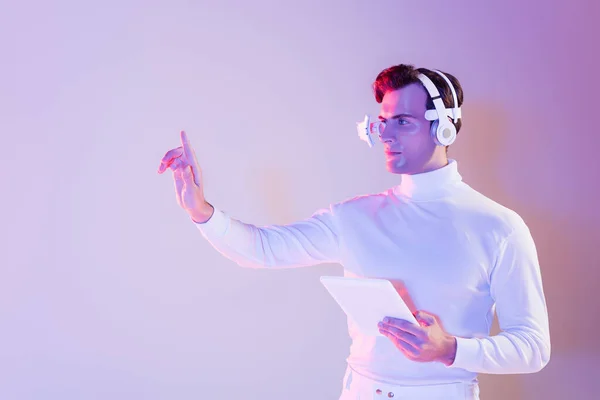 Cyborg in headphones holding digital tablet and using something on purple background — Stock Photo
