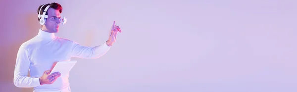 Кіборг людина в навушниках використовує щось, тримаючи цифровий планшет на фіолетовому фоні, банер — стокове фото