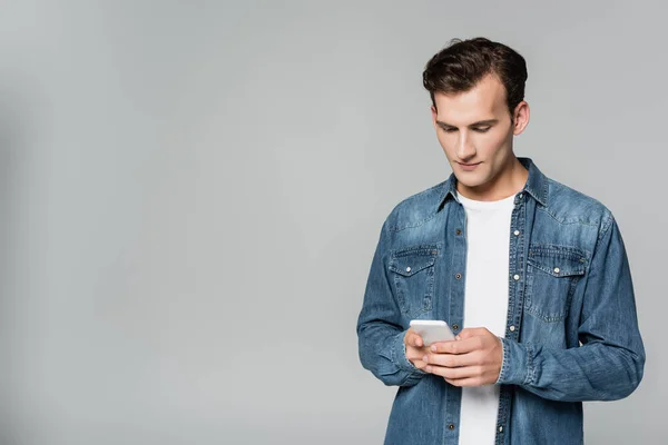 Jeune homme veste en denim en utilisant smartphone isolé sur gris — Photo de stock