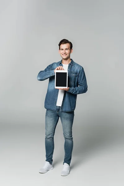 Smiling man in denim jacket holding digital tablet with blank screen on grey background — Stock Photo