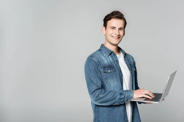 Homme joyeux en jean veste en utilisant ordinateur portable isolé sur gris — Photo de stock