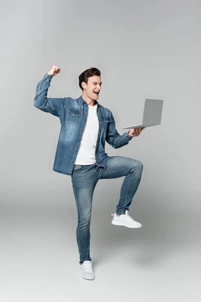 Веселый человек показывает да жест, держа ноутбук на сером фоне — стоковое фото