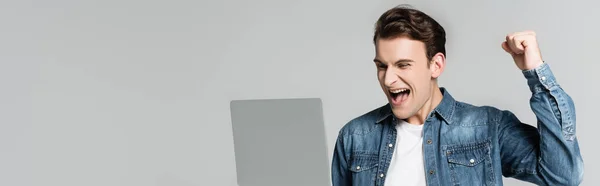 Positiver Mann zeigt Ja-Geste beim Blick auf Laptop isoliert auf grau, Banner — Stockfoto