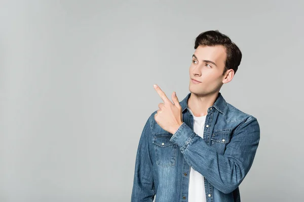 Junger Mann in Jeansjacke zeigt mit Finger auf Grau — Stockfoto