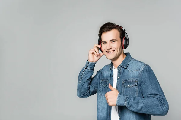 Hombre alegre en auriculares mostrando como gesto aislado en gris - foto de stock