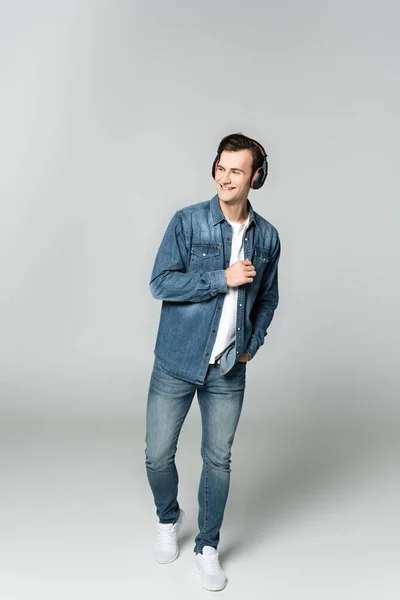 Веселый мужчина в джинсовой куртке и наушниках на сером фоне — стоковое фото