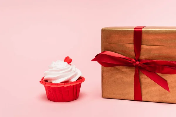 Cupcake de San Valentín con corazón rojo cerca de regalo sobre fondo rosa - foto de stock