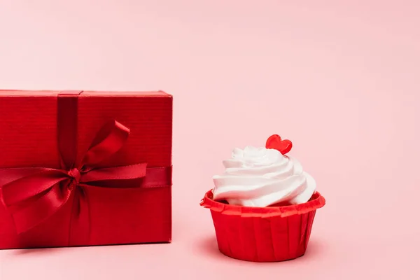 Cupcake de San Valentín con corazón rojo cerca de regalo sobre fondo rosa - foto de stock