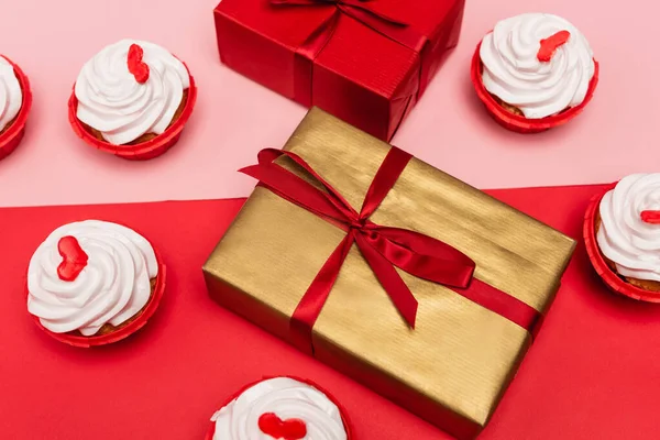 Cupcakes de Saint-Valentin près de boîtes-cadeaux sur fond rose et rouge — Photo de stock