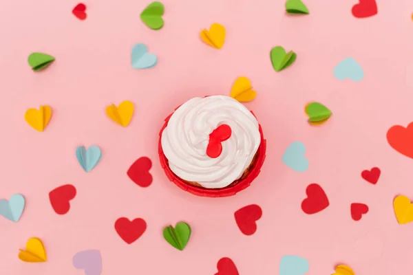 Top view of colorful paper hearts and cupcake on pink background — Stock Photo
