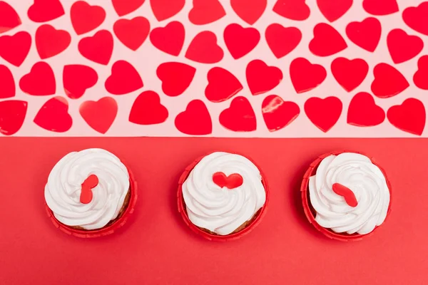 Draufsicht auf Herzen und Cupcakes auf rotem und rosa Hintergrund — Stockfoto